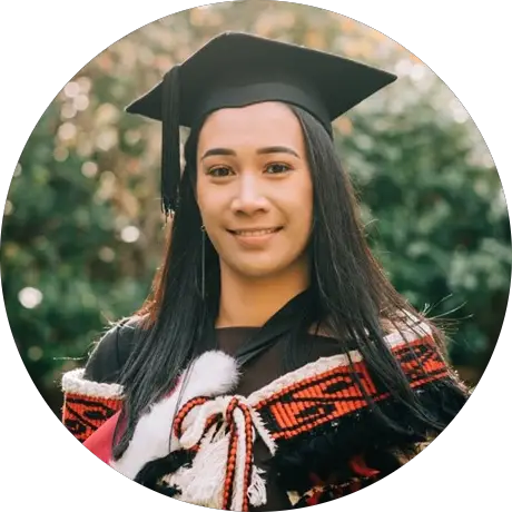 Sade is a young Māori wahine. She is facing the left, wearing a graduation cap and gown, with a korowai over the top. The korowai has koru detailing around the top, and is primarily black, red and white. .